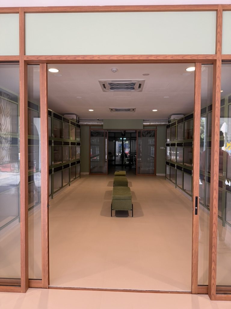 The entrance hall, looking in through wooden-framed glass doors, with cages along both walls and green seating down the middle