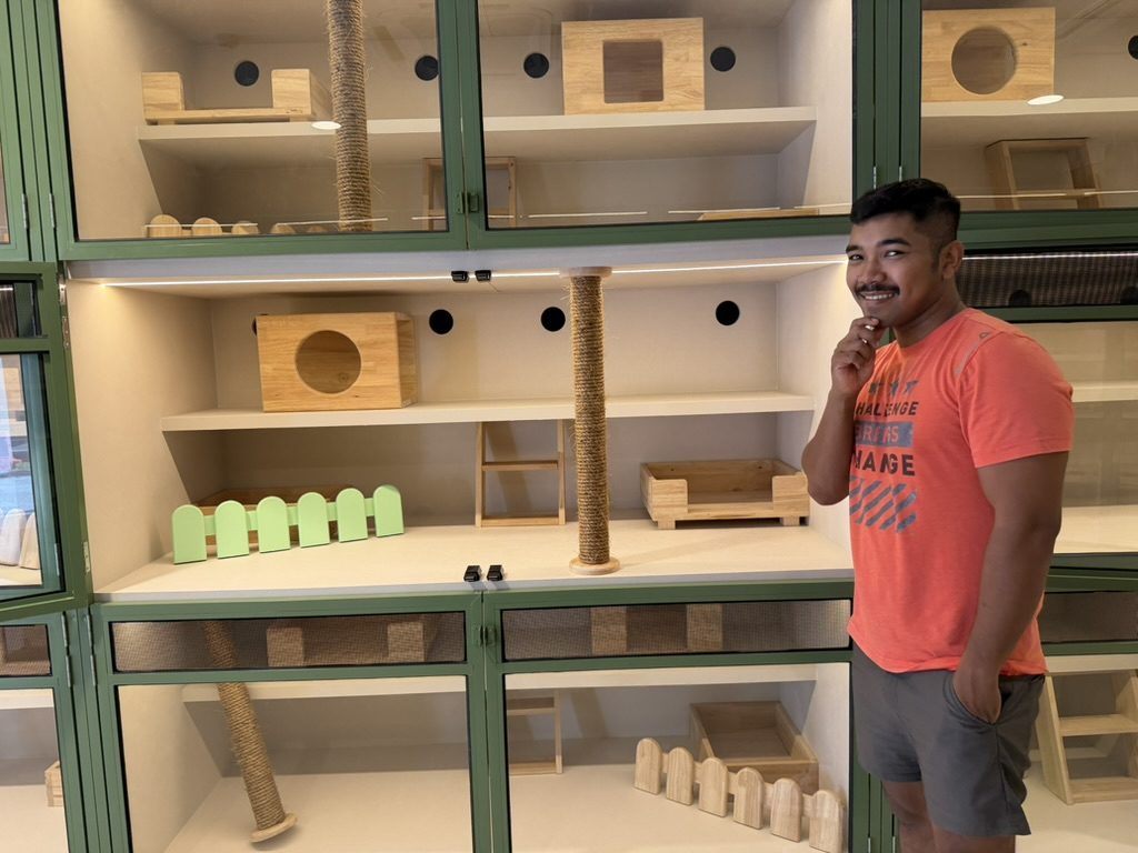 A team member beside a green-framed glass cage with shelves, a climbing post and a wooden den